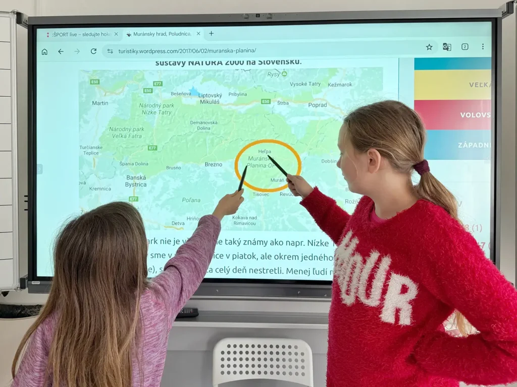 Dve žiačky ukazujú na interaktívnej tabuli Muránsku planinu na mape Slovenska počas hodiny zemepisu